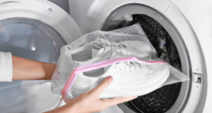 Woman putting mesh with white sneakers into washing machine, closeup